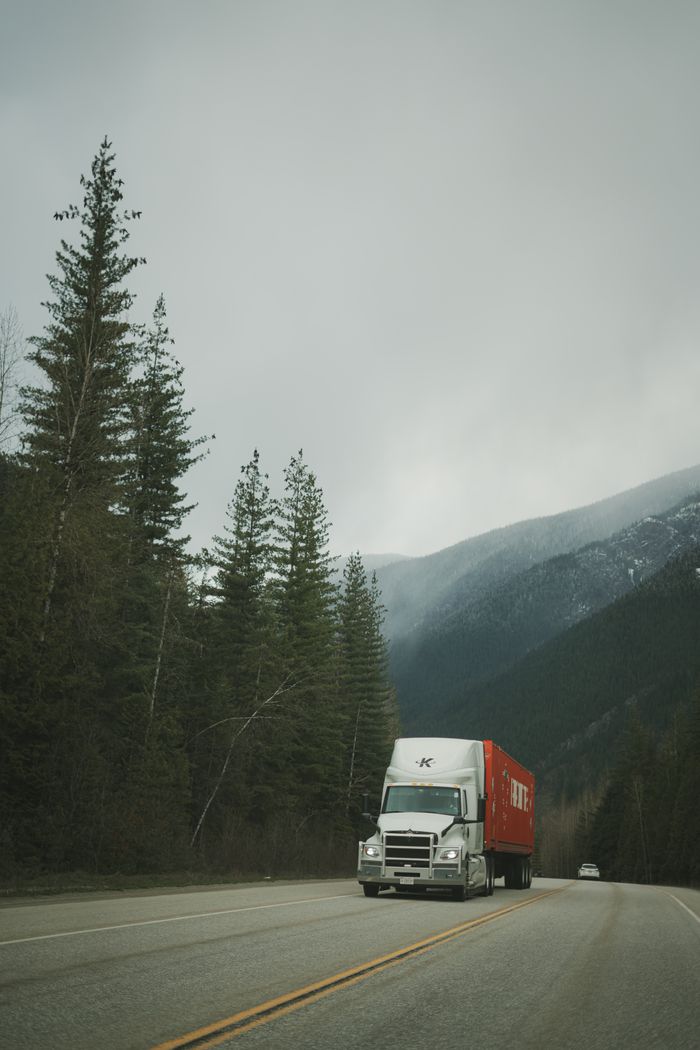 Services A delivery truck drives along a scenic highway surrounded by mountains and evergreen trees.